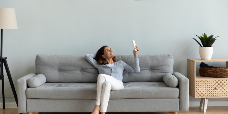 woman sitting on couch holding air conditioner remote